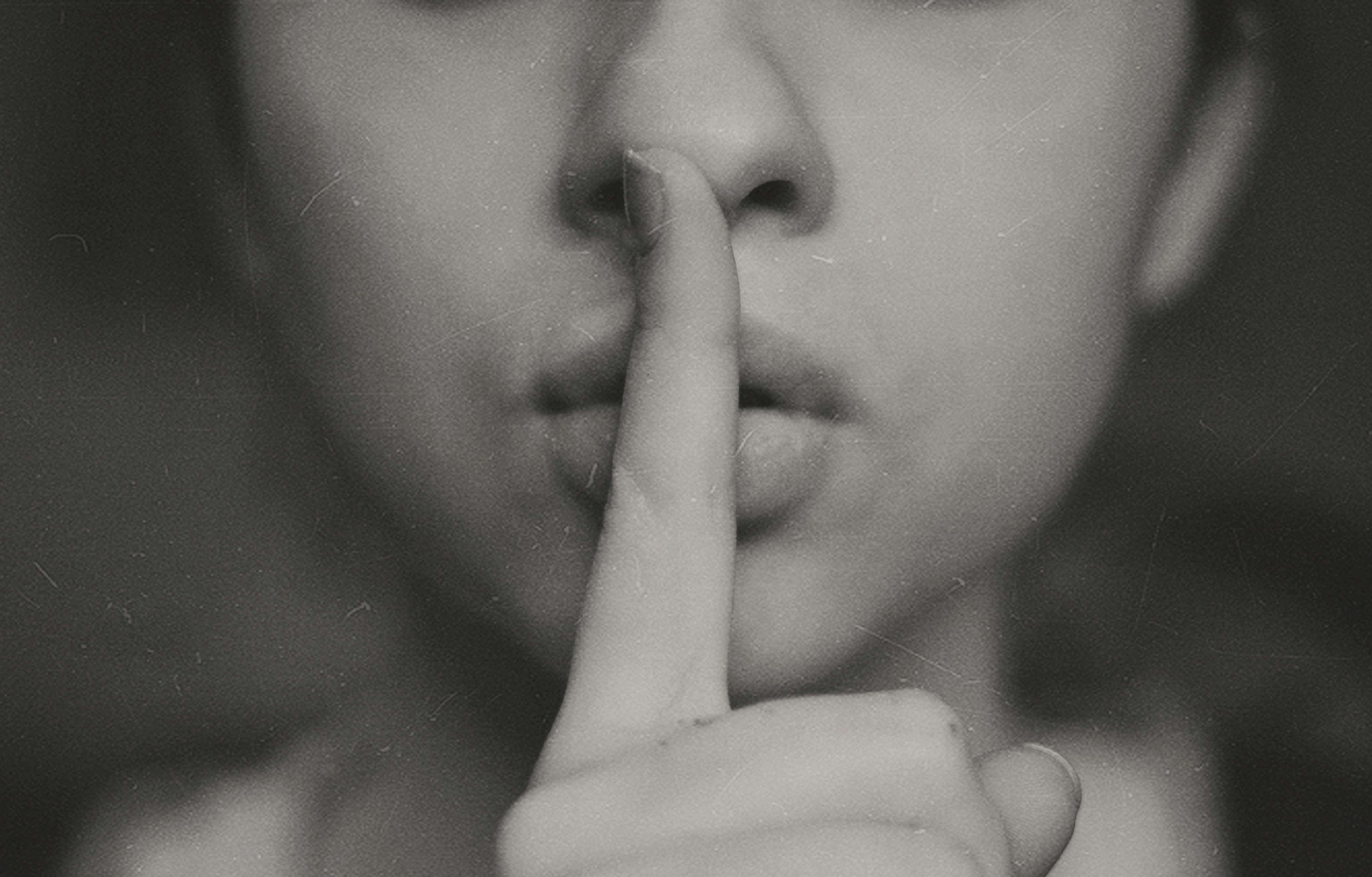 口元に指を当てて静かにしている女性のモノクロ画像